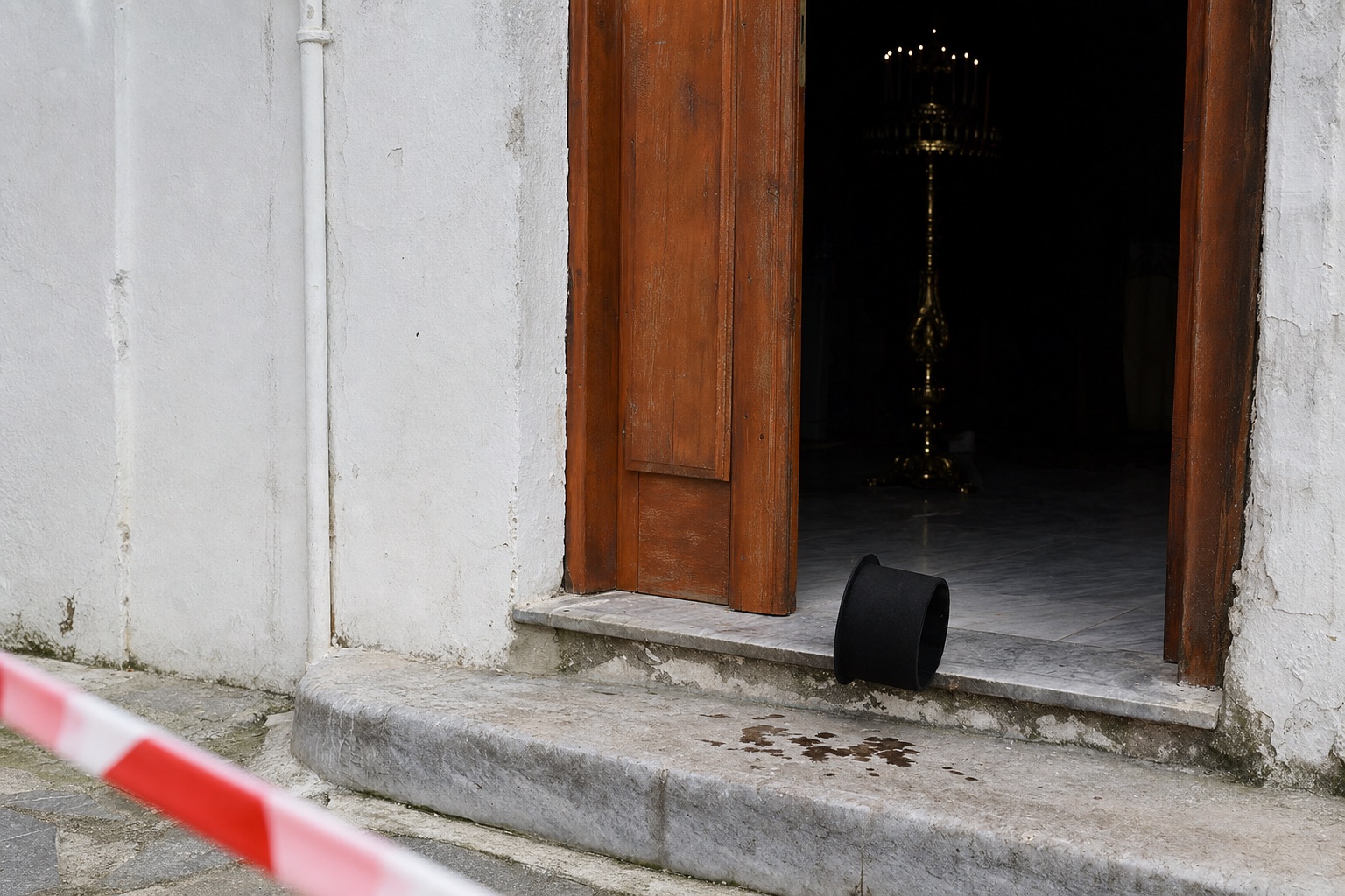 Η ανοιχτή πόρτα του καθολικού με το καλυμμαύχι του ιερέα πεσμένο στο σκαλοπάτι και κορδέλα της αστυνομίας